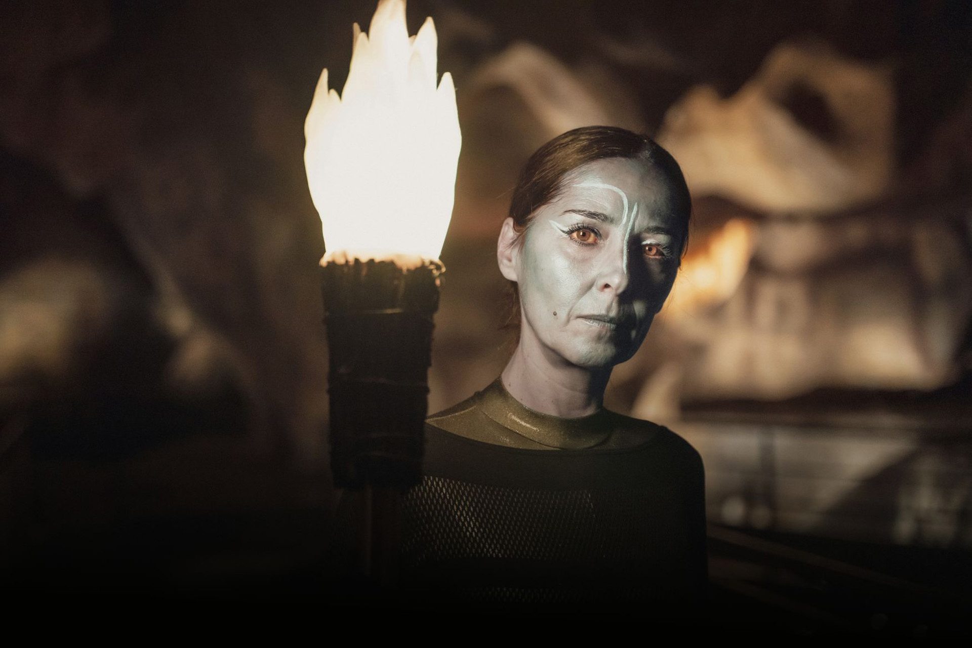 Pièce de théâtre l'Œil de Dieu - Une femme le visage maquillé de bleu tient une torche dans sa main, dans la grotte restituée.